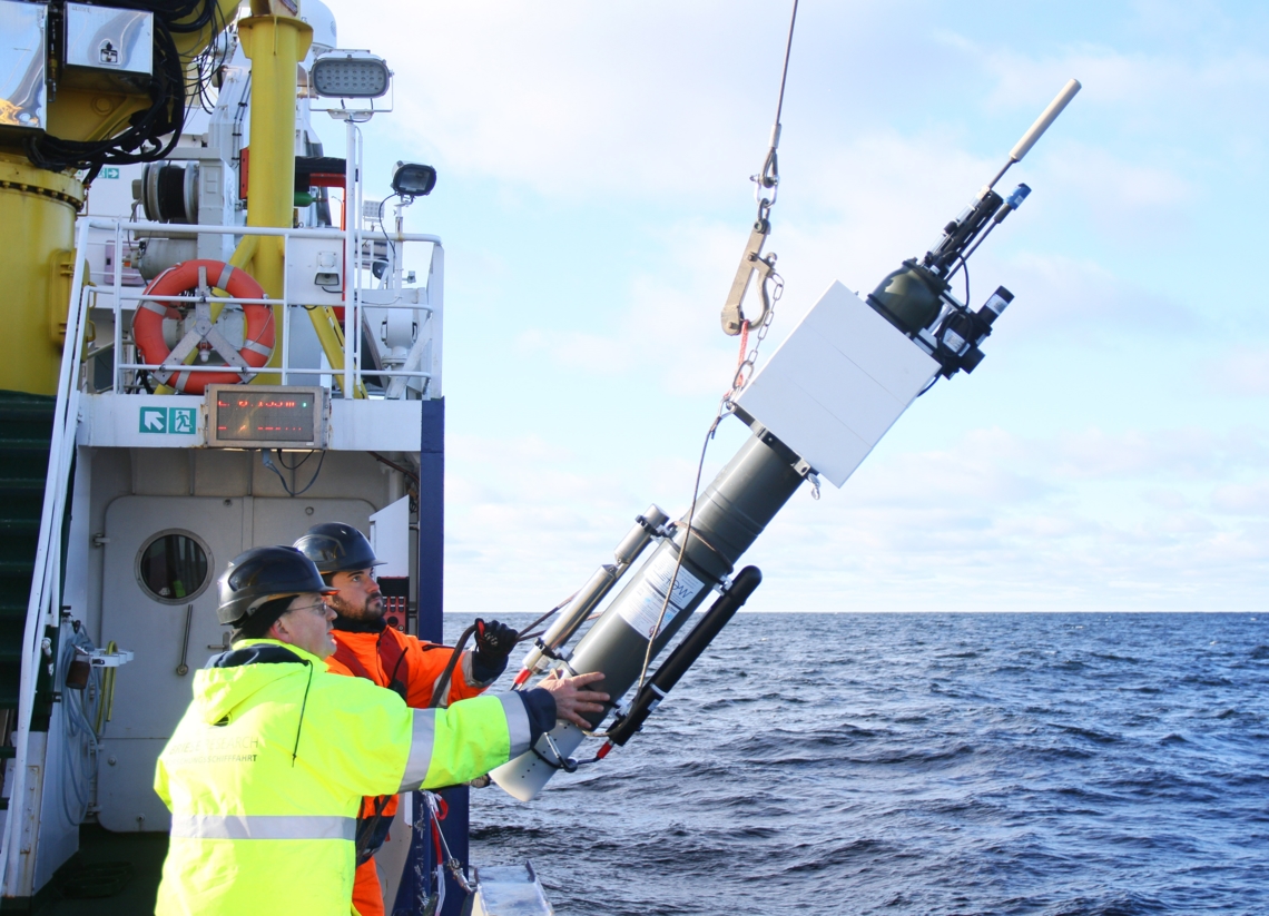 Two people lower a biogeochemical profiling float in the water from the side of a boat