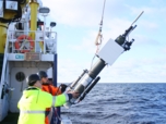 Two people lower a biogeochemical profiling float in the water from the side of a boat